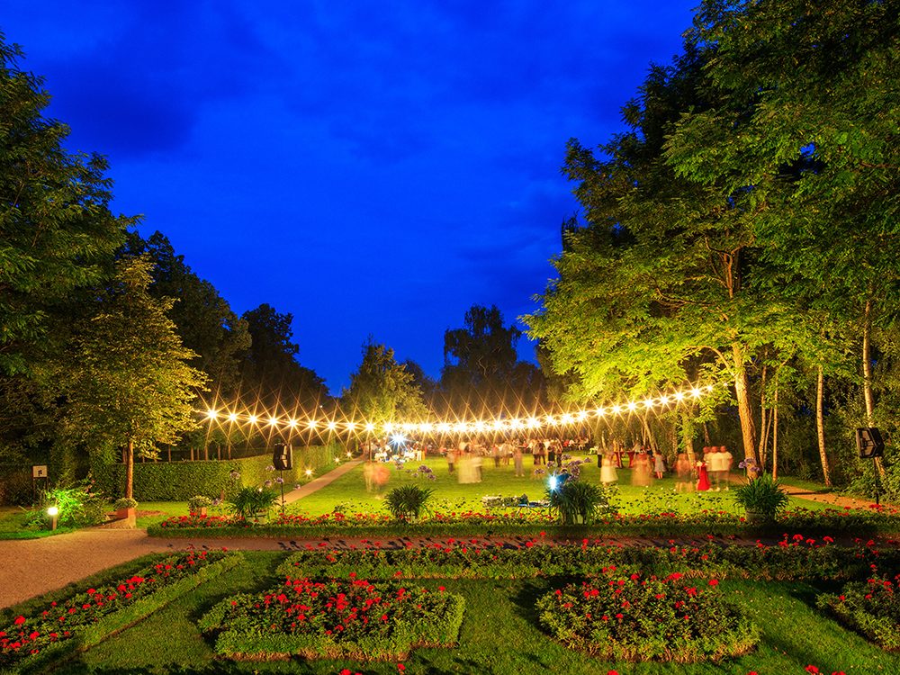 Der Garten der Liebermann-Villa am Abend. Über der Wiese leuchtet eine Lichterkette.