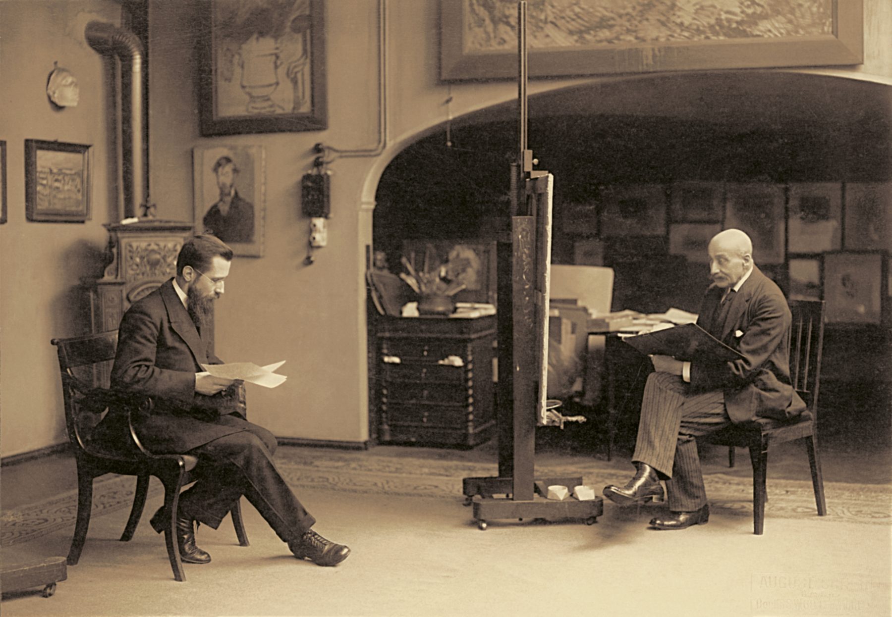 Zwei Künstler Max Liebermann und Fritz Heyder sitzen sich gegenüber, zwischen ihnen steht eine Staffelei