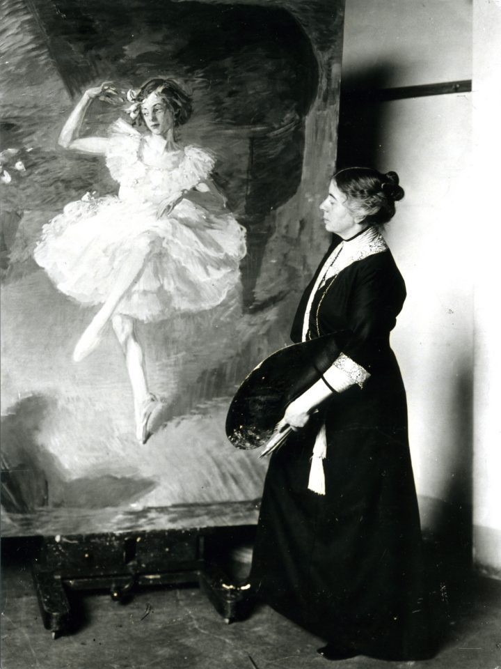 Eine Künstlerin im Kleid mit Hochsteckfrisur steht vor einem lebensgroßen Gemälde eines tanzenden kleinen Mädchens, in der linken Hand hält die Malerin Pinsel und die Farbpalette