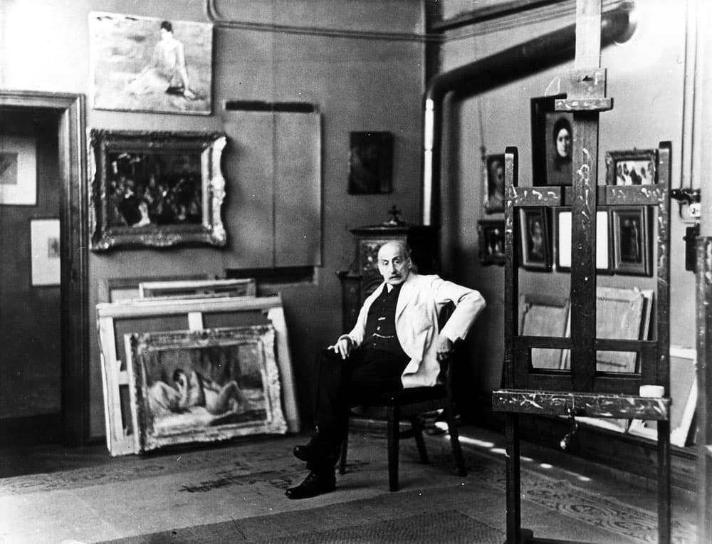 Auf dieser Fotografie von 1931 sitzt der Maler Max Liebermann in seiner Atelier am Pariser Platz. Im Vordergrund steht eine leere Staffelei, an den Wände hängen diverse Ölbilder des Künstlers. Hinter Ihm in der hängt über den Kamin die Liebermann St. Adriansschützen nach Frans Hals.