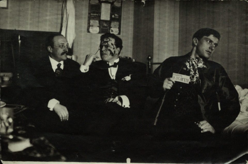 Schwarz-Weiß-Fotografie von drei sitzenden Männern in eleganten Kostümen.