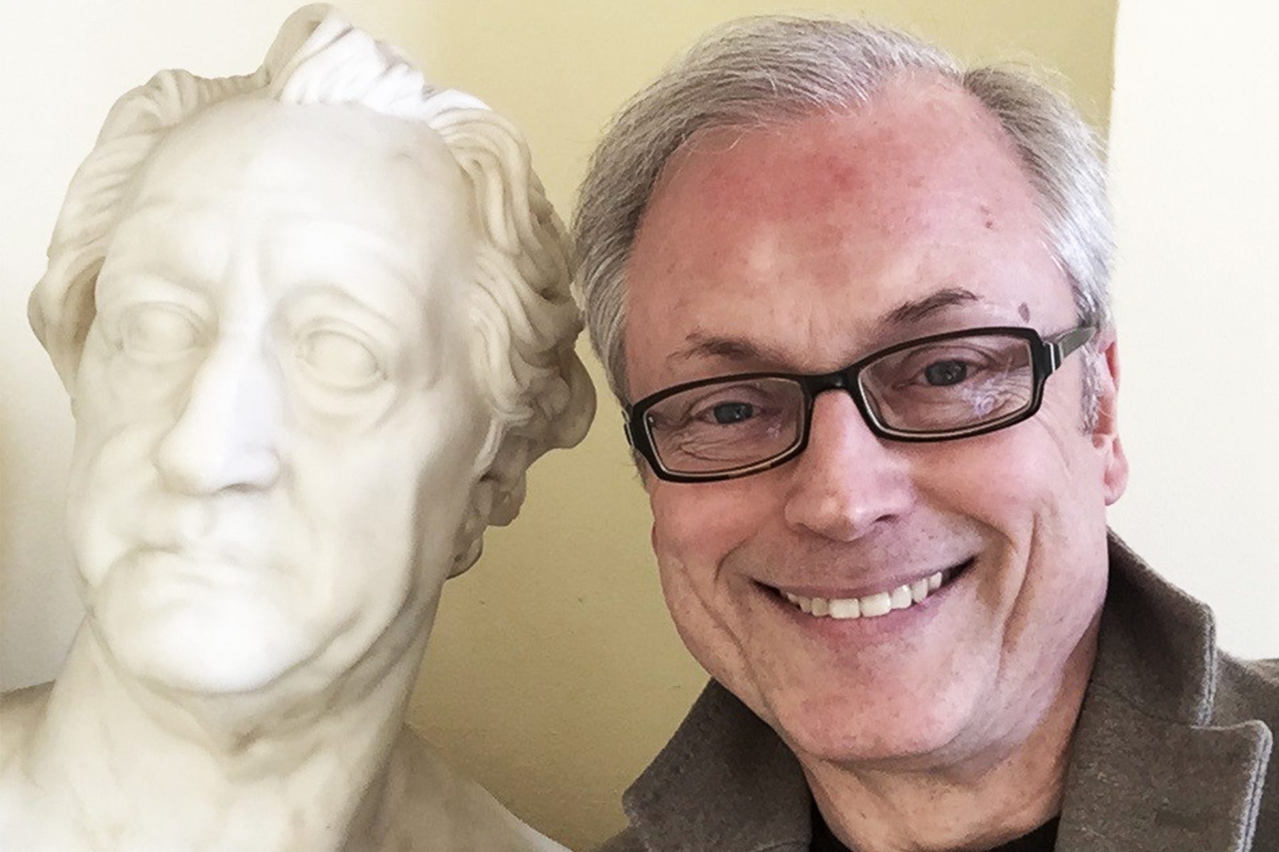 Links ist eine weiße Marmorskulptur des Kopfes eines älteren Goethes. Rechts blickt ein Mann freundlich in die Kamera, er trägt eine Brille.