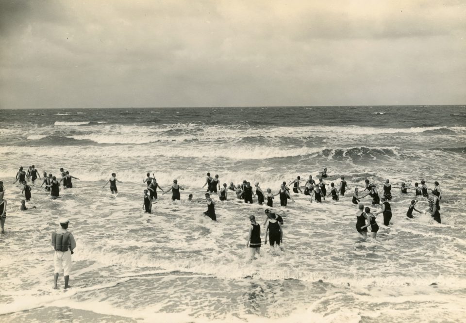 Auf dem historischen Foto baden viele Personen mit Badeanzügen im Meer