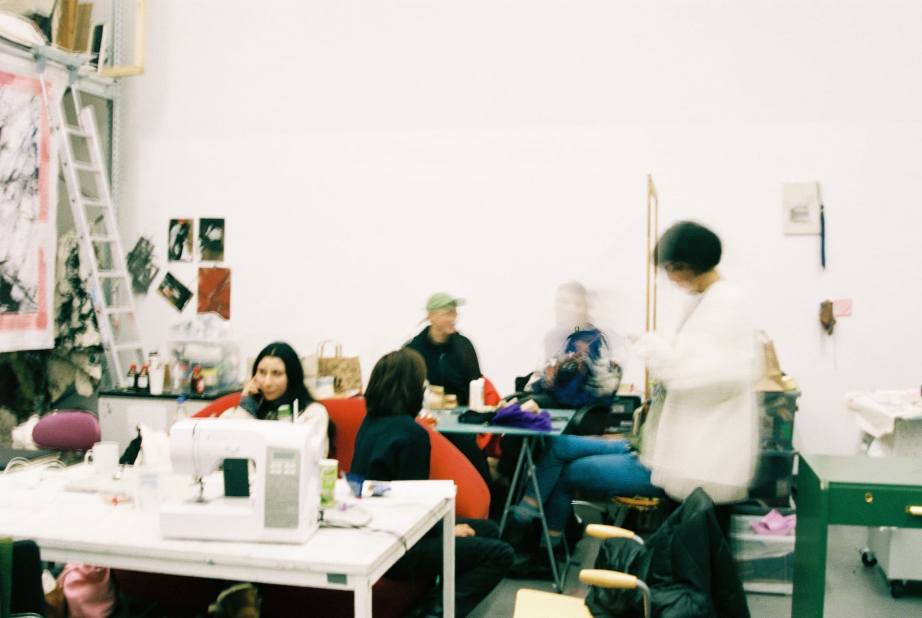 Foto eines Ateliers mit mehren Personen an Tischen, stehend und in Bewegung.