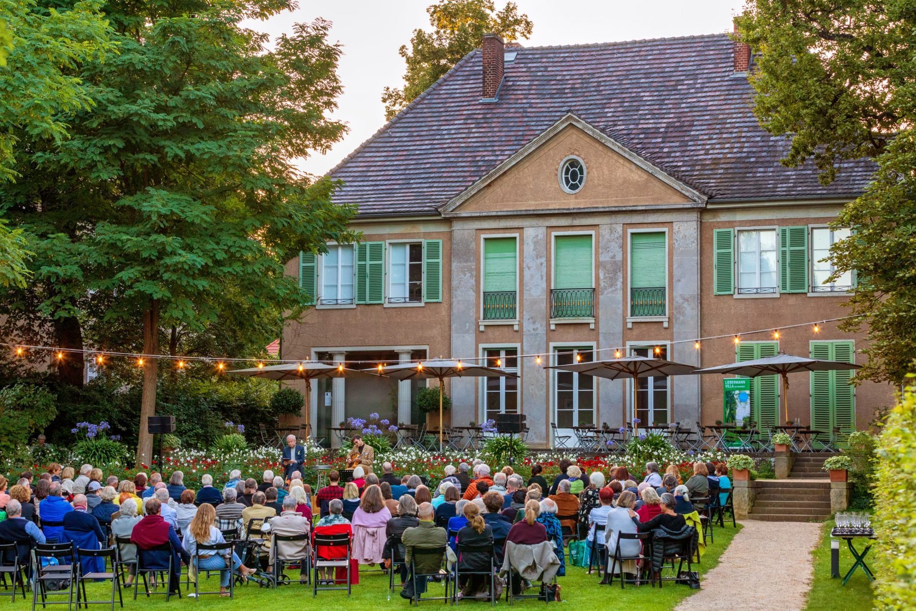 Foto einer Konzertlesung im Garten der Liebermann-Villa mit vielen Personen im Publikum und zwei Künstlern.