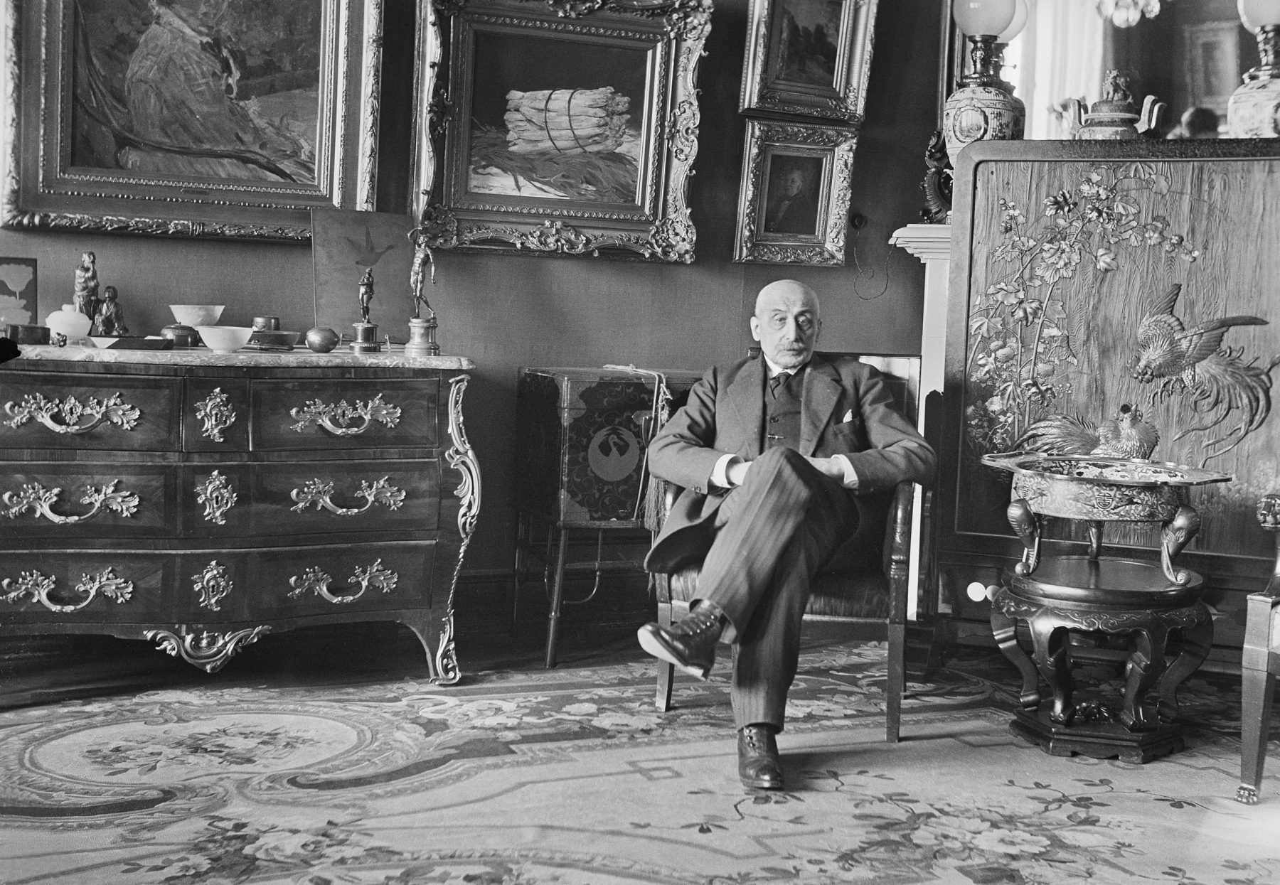 Fotografie von Max Liebermann in seiner Wohnung am Pariser Platz. Er sitzt auf einem Sesse, im Hintegrund sind kostbare Möbelstücke und Kunstwerke.