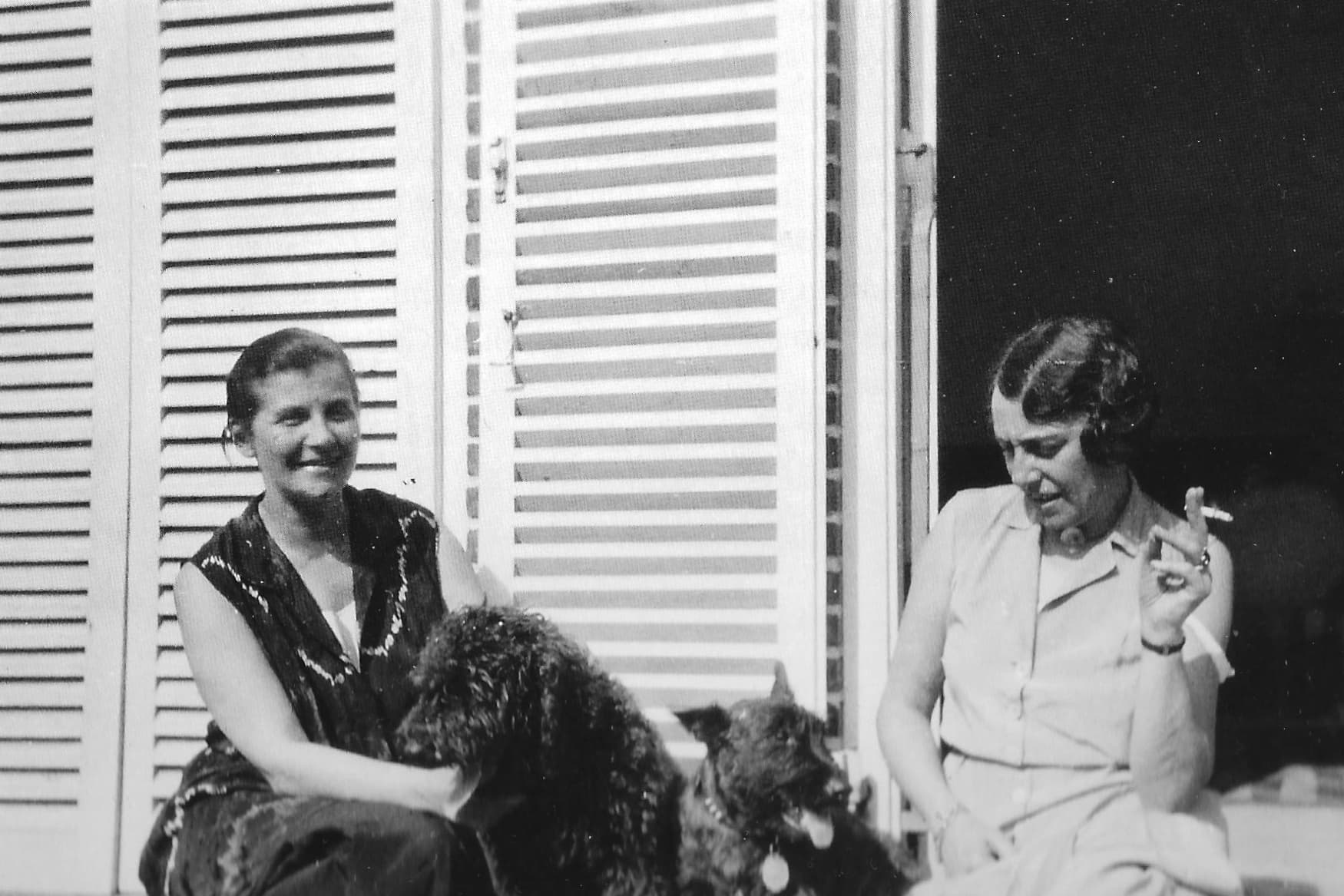 Historisches Schwarzweißfoto von zwei Frauen sitzend vor einem Gebäude