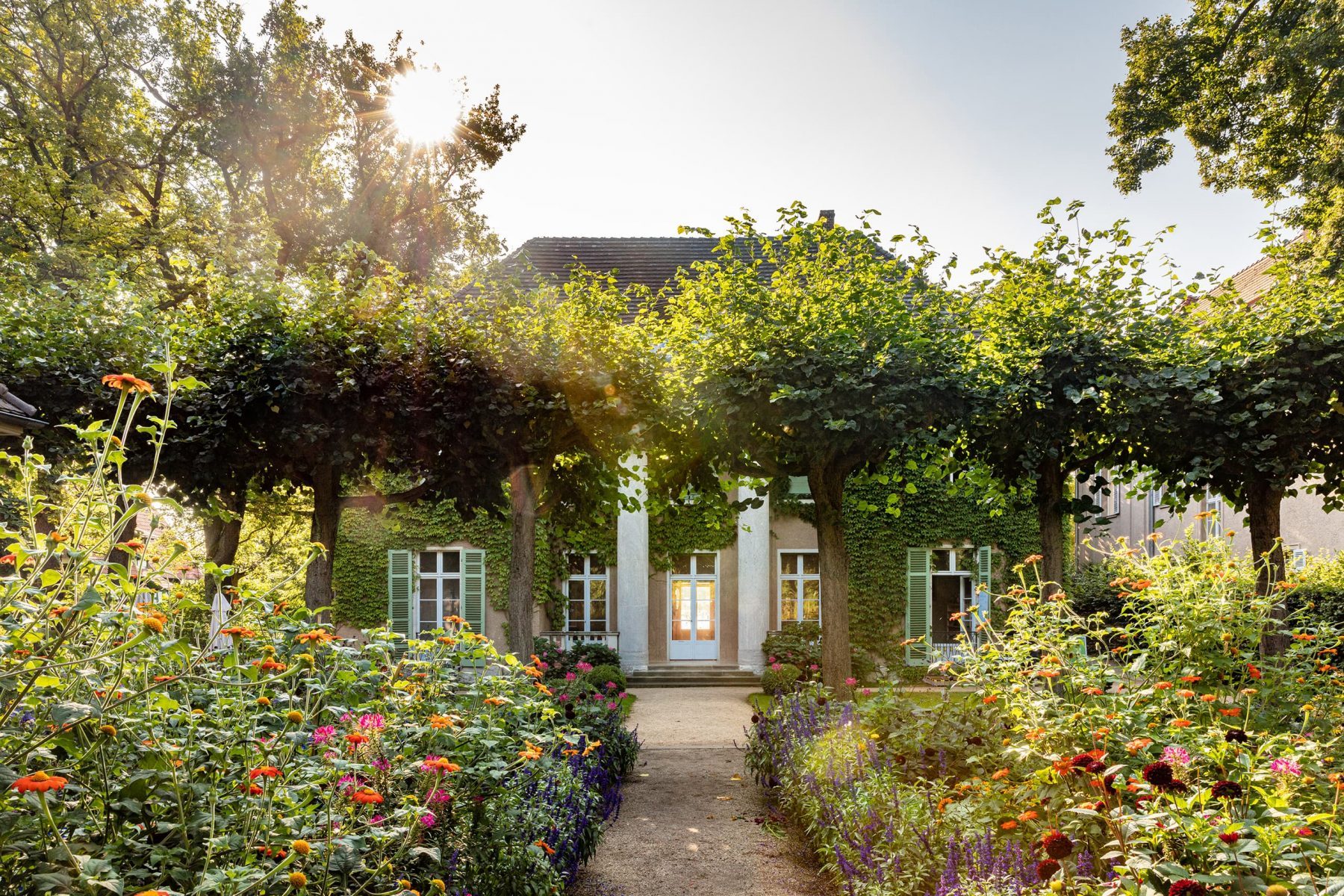 Mit Wein bewachsene Frontseite der Liebermann-Villa mit vielen bunten Pflanzen und hohen Bäumen